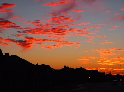 [Above the dark rooftops are yellow-orange clouds on the right(closest to the sun) and orange-pink-purple clouds to the left.]